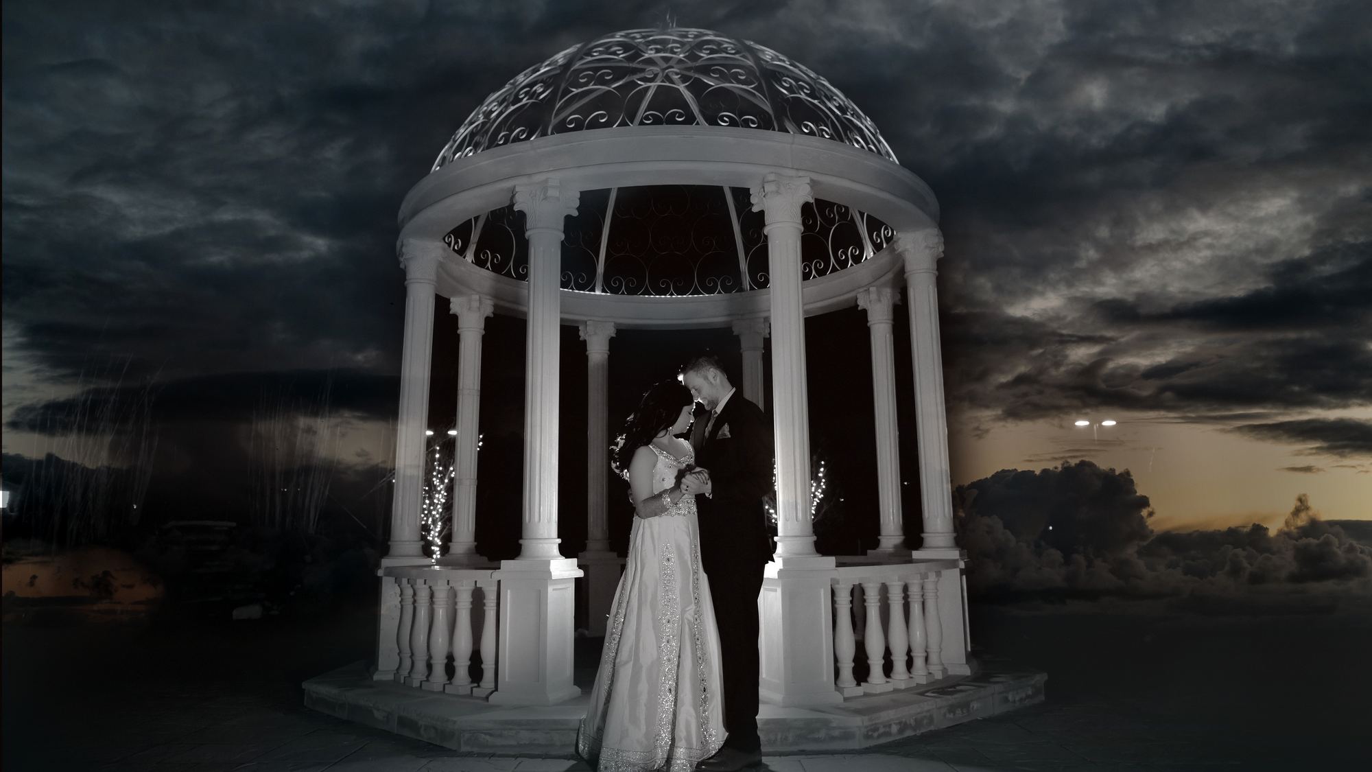A bride and groom beneath a lit gazebo at dusk