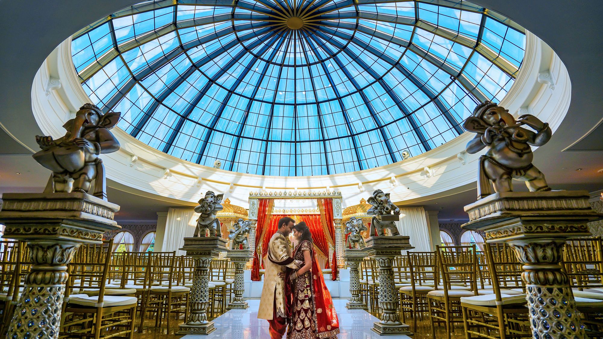 A bride and groom beneath a glass dome in a decorated ceremony hall