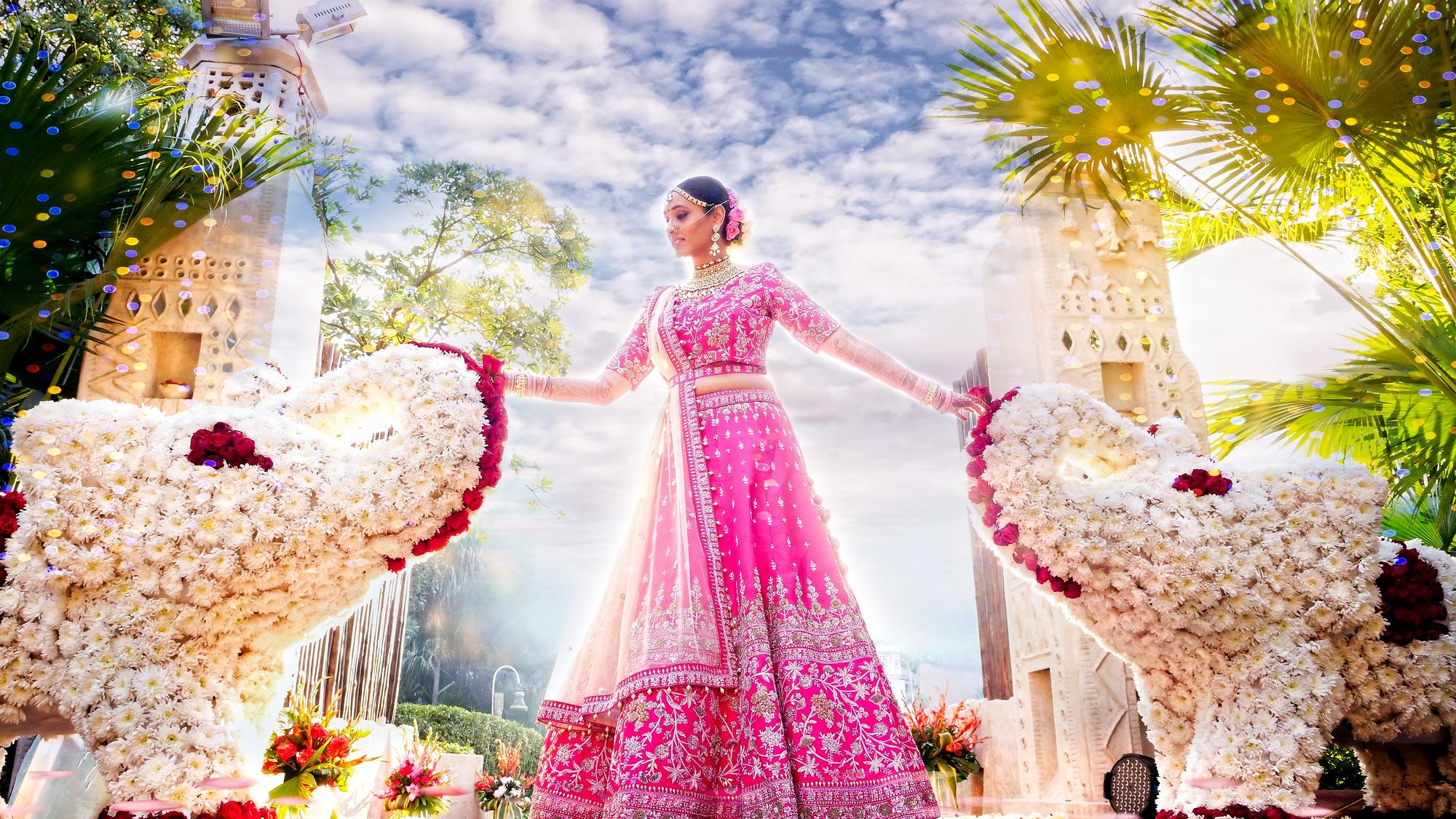 A bride in a pink lehenga on a flower-lined walkway
