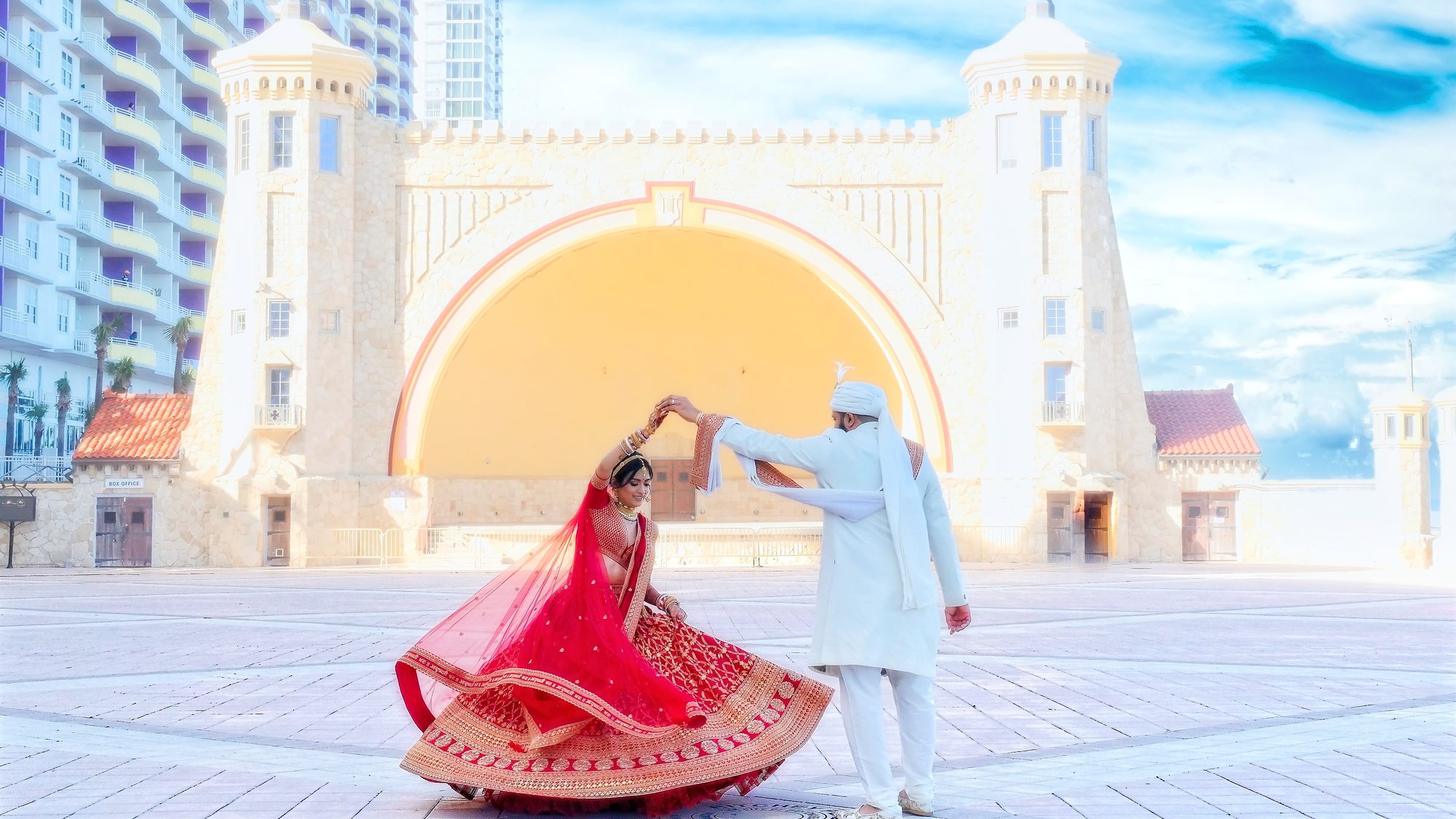 A groom twirling his bride in front of a grand amphitheater