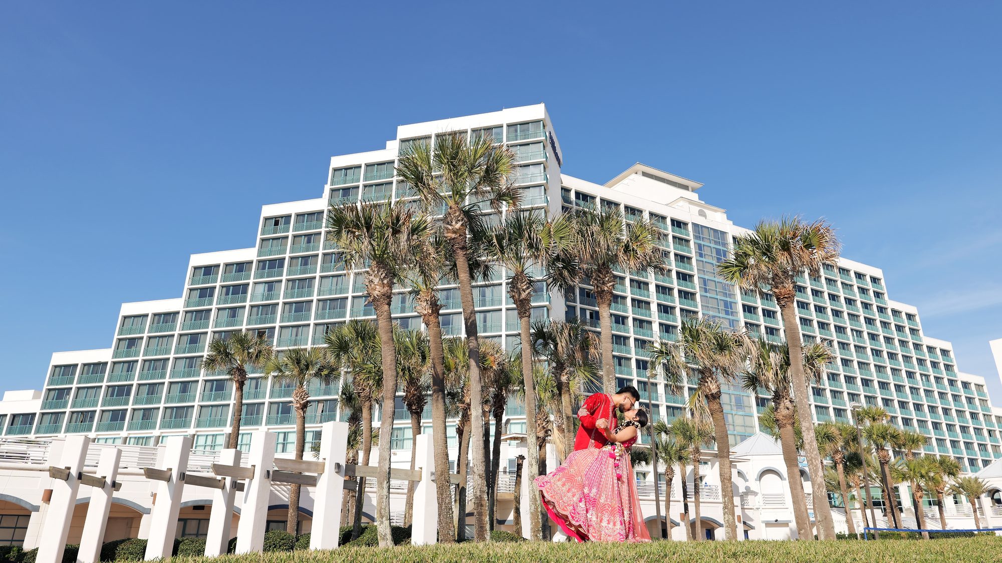 A bride and groom beneath palm trees outside a beachfront resort