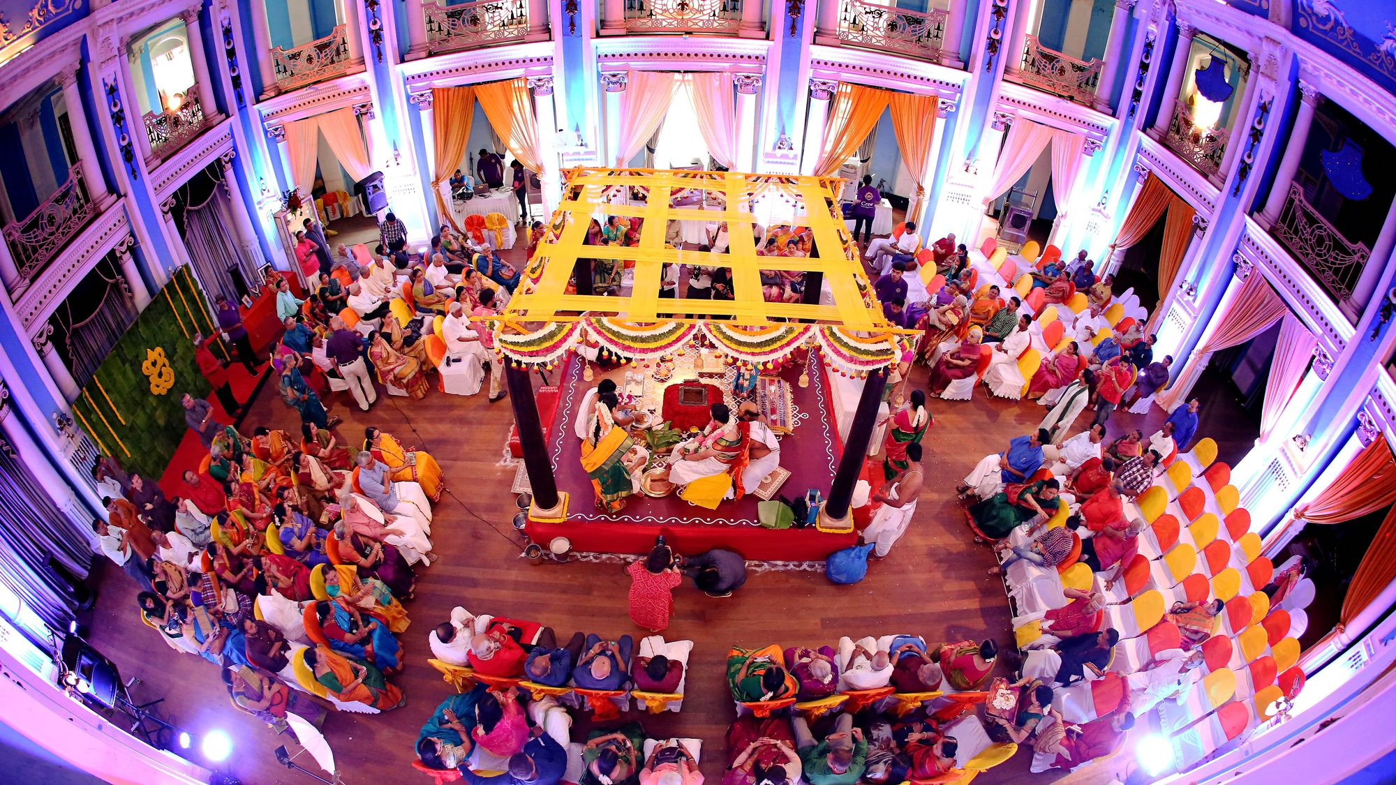 An overhead view of a ceremony hall filled with guests around a decorated mandap